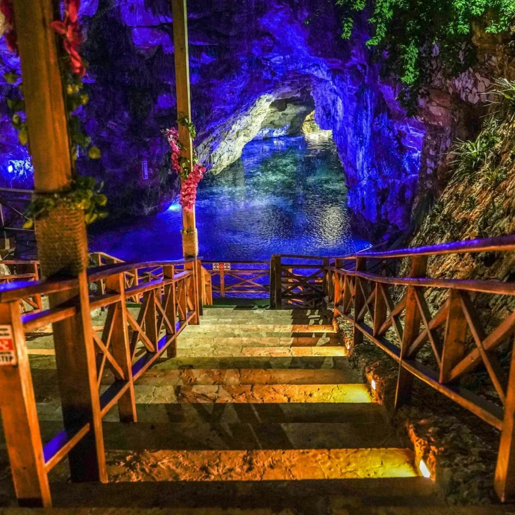 Stairs leading to a vibrant cave pool in Miches, illuminated by colorful lights, perfect for adventure seekers.